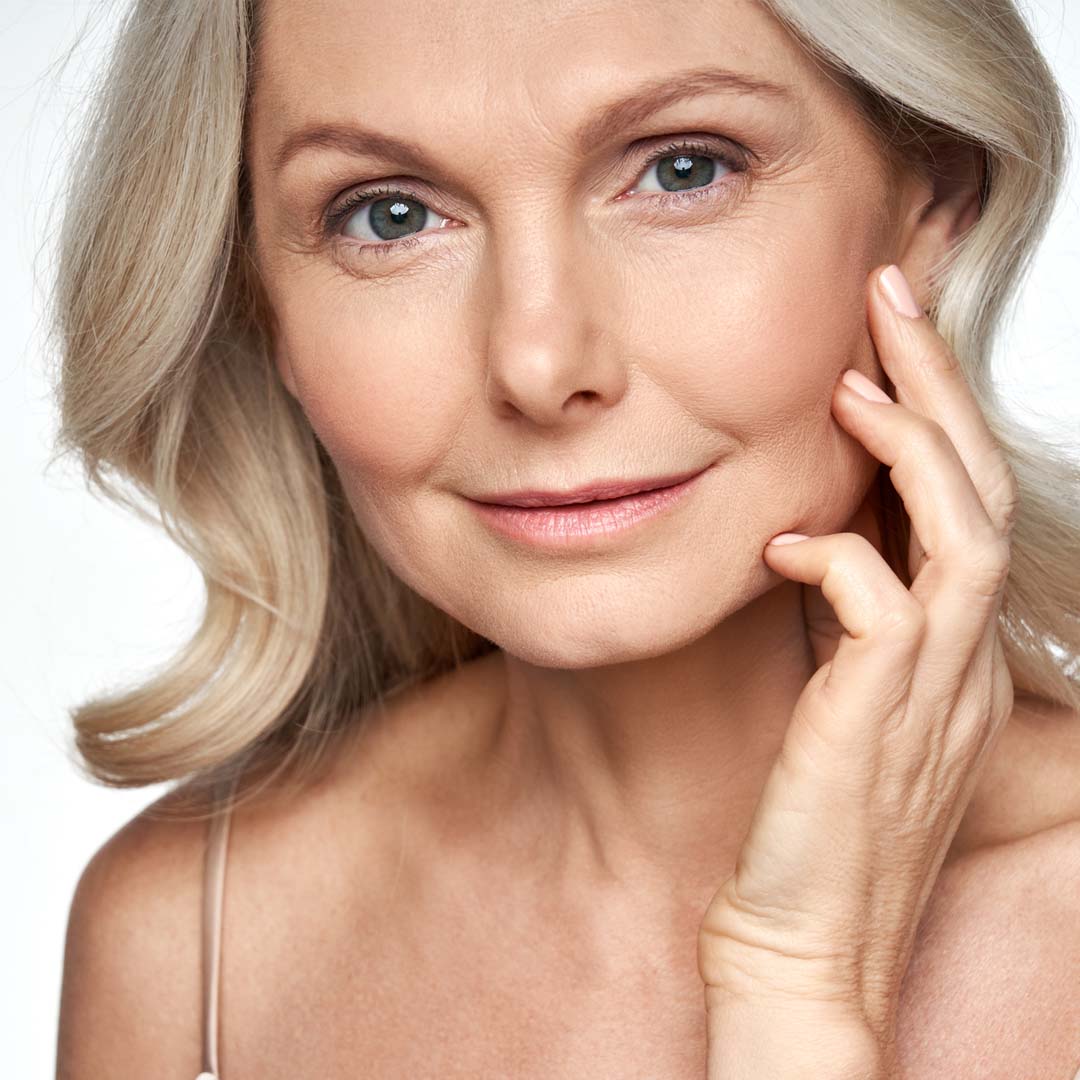 A mature woman smiling and touching her face