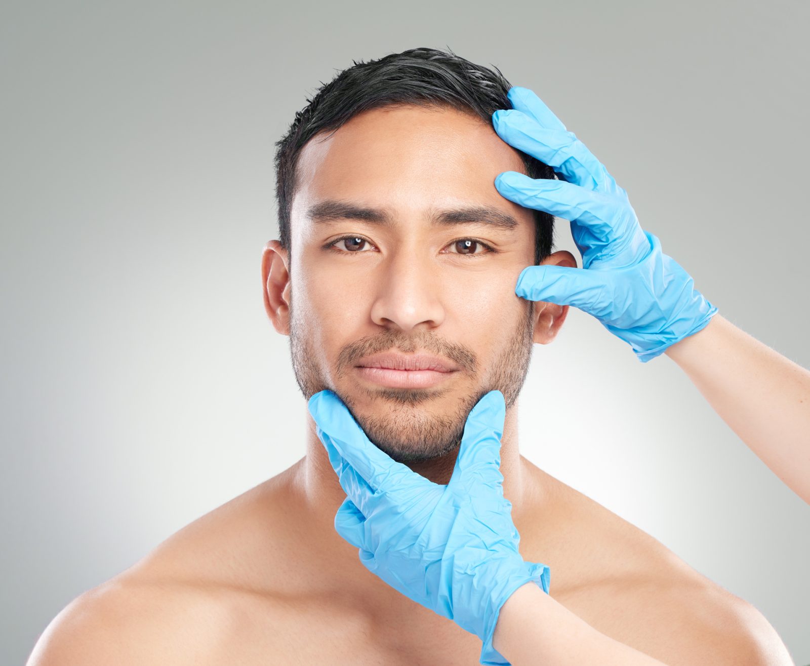 Studio portrait of a handsome young man having his face examined against a grey background