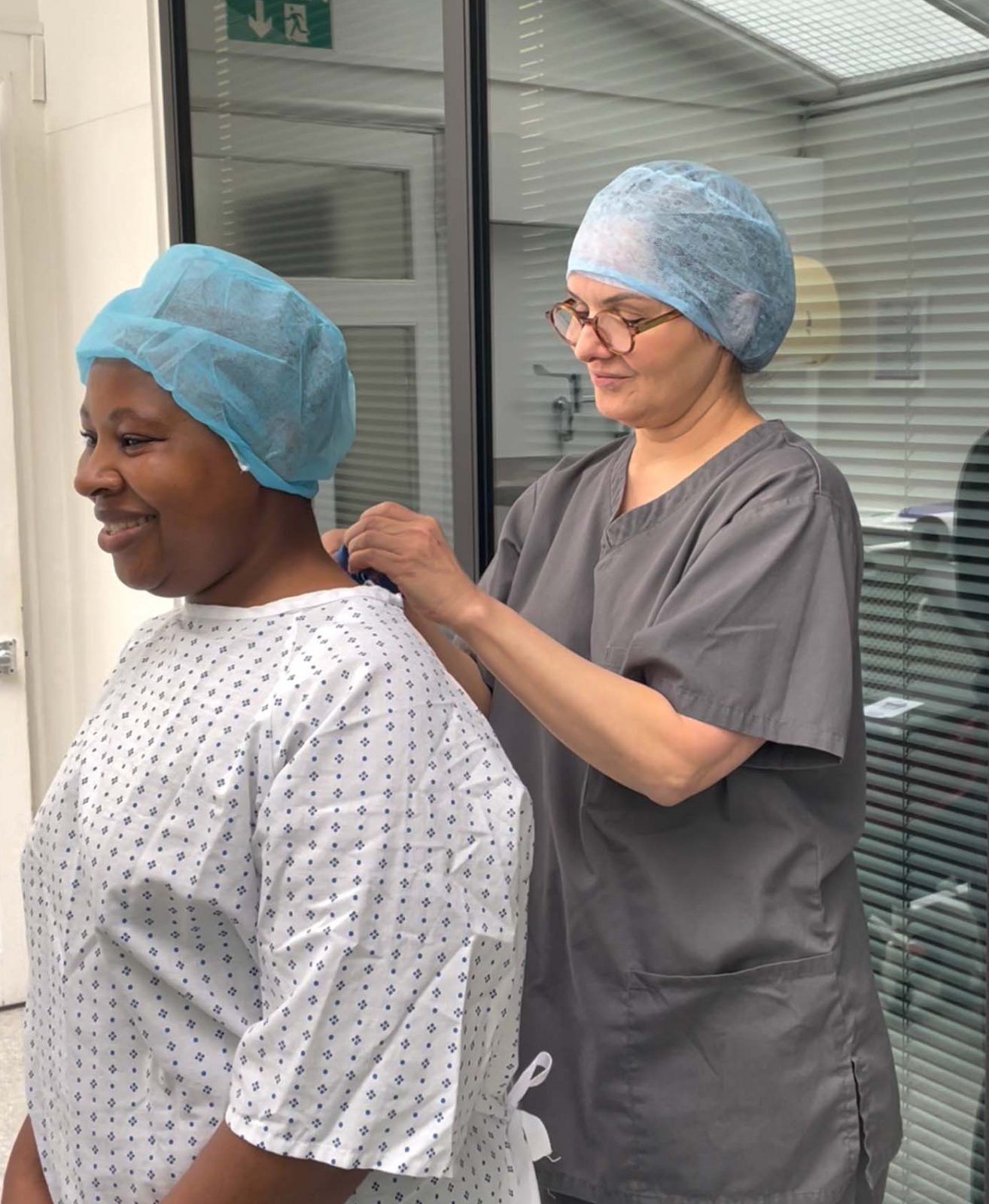 A nurse is helping a patient put on a surgical gown