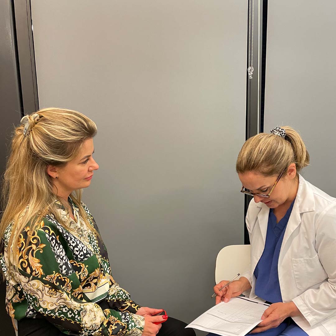 A nurse sits across from a woman and is filling out a form