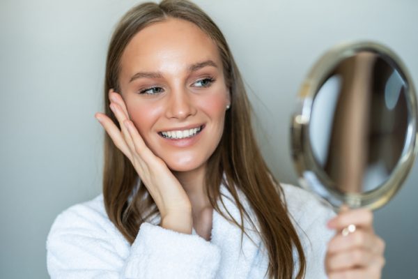 Beautiful young woman with a clean fresh skin touches with a hand a cheek